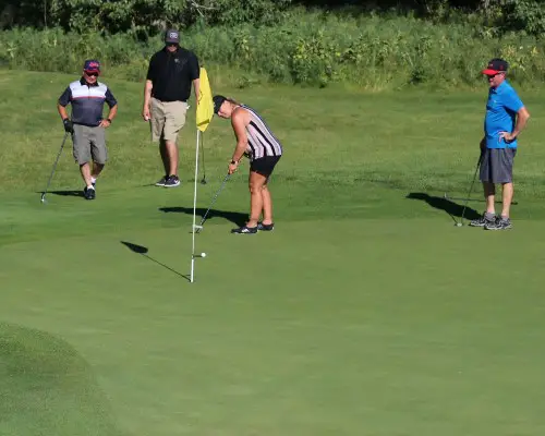 A group of people competing in a Dirty Golf Tournament on a green.