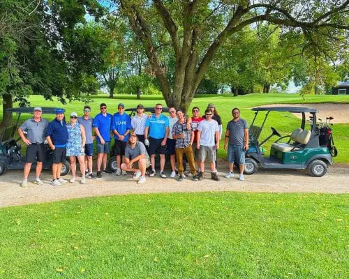 A group of people posing for a photo at a funny golf tournament event on a golf course.