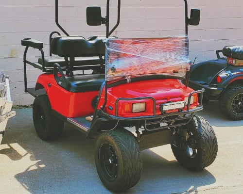 A red golf cart parked in front of a garage with installed headlights.