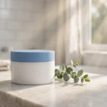 A plain blue and white moisturizer tub on a bright bathroom counter in morning sunlight